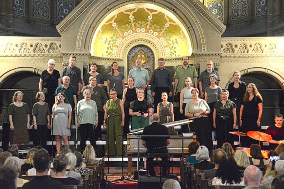 Bild: Gospelchor True Note auf der B�hne vor dem Altar in bunter Kleidung singend mit Chorleiter Stefan Bechstein am Klavier.